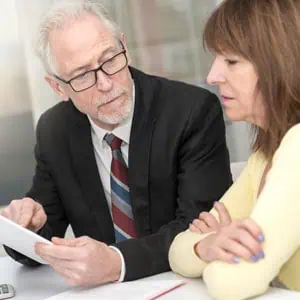 Older man explaining trust administration details to a woman using a tablet during a meeting