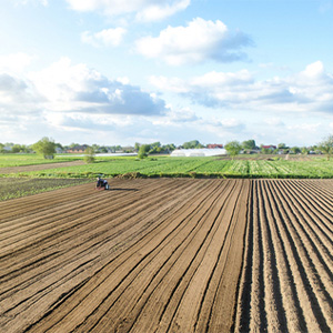 Wide view of a tractor plowing parallel rows in a large farm field.